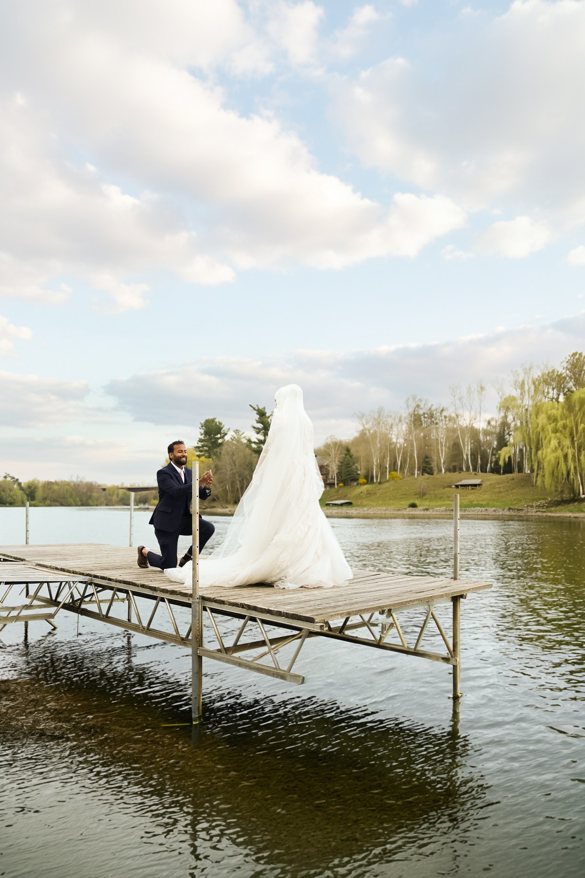 Groom kneeling for bride on a lakeside dock