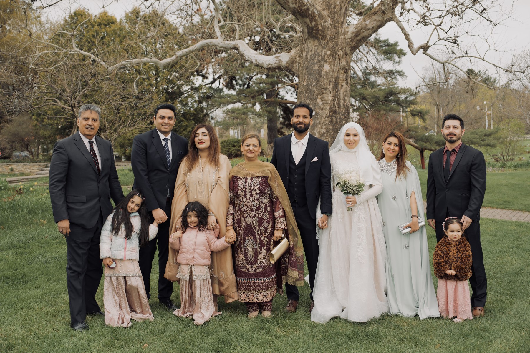 Bride and groom surrounded by family under a tree