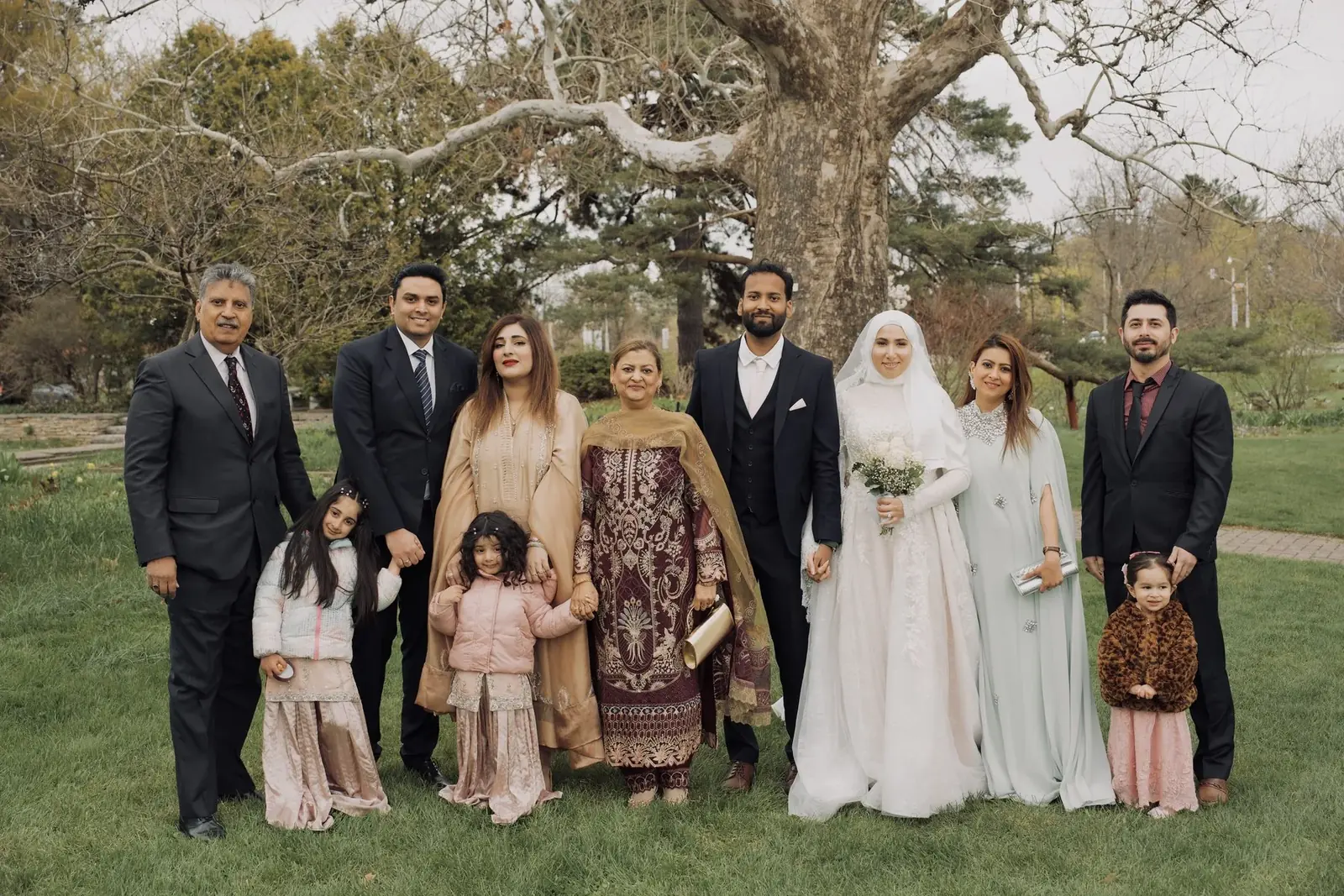 Bride and groom surrounded by family under a tree