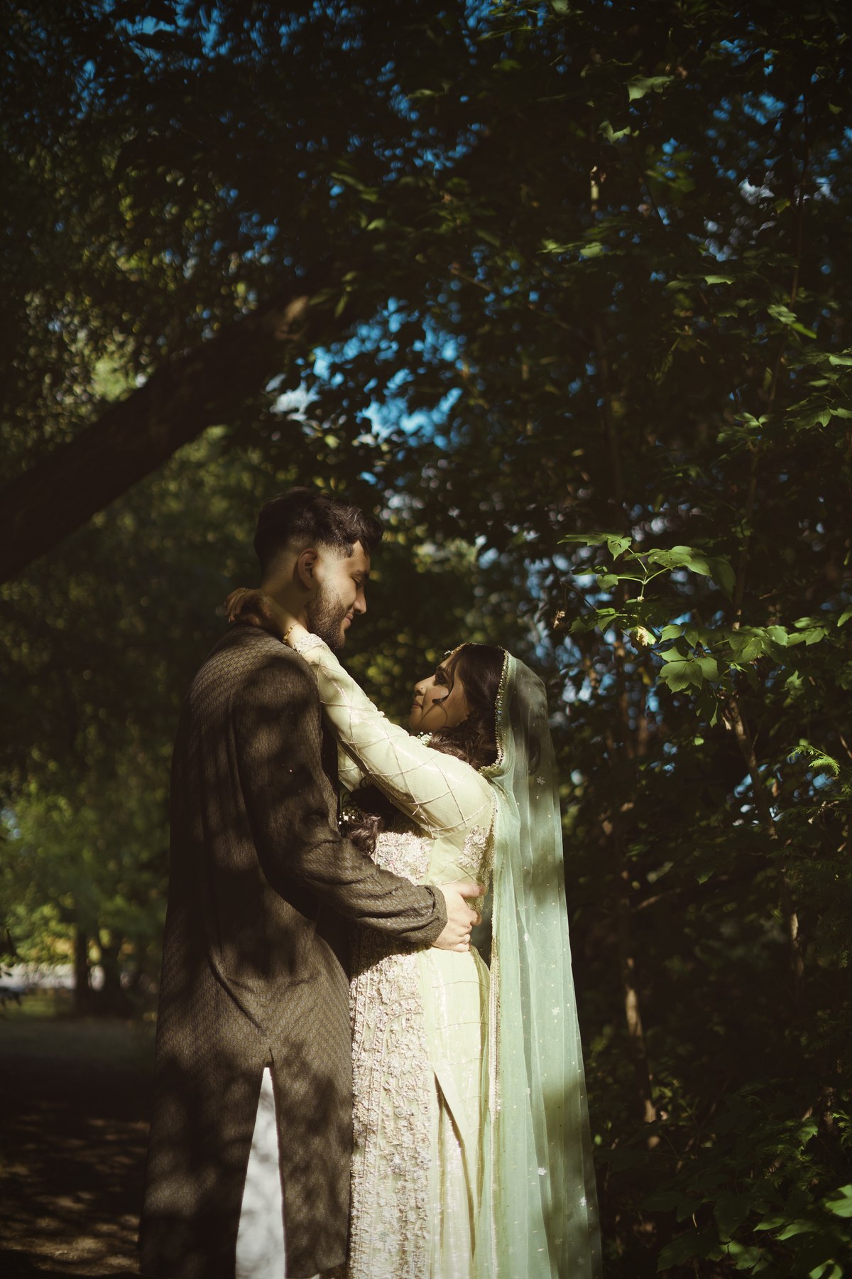 Bride and groom embracing beneath forest trees