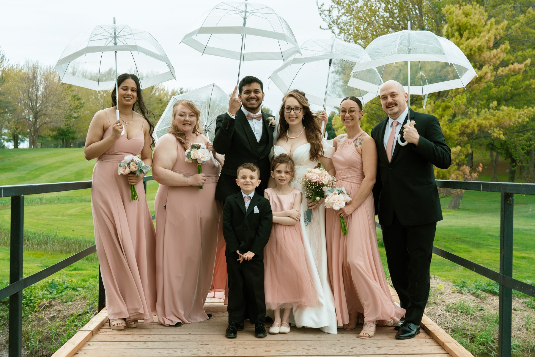 Bride, groom, and wedding party holding clear umbrellas in the rain